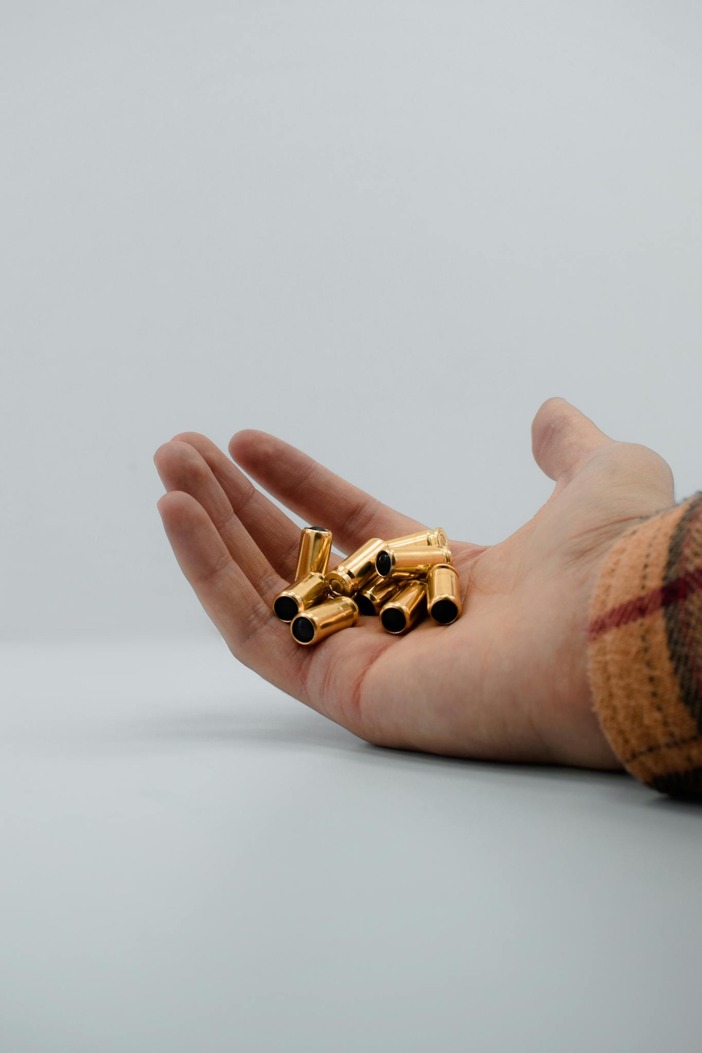 A hand holds several golden bullet casings against a plain white backdrop, showcasing details in a vertical shot.