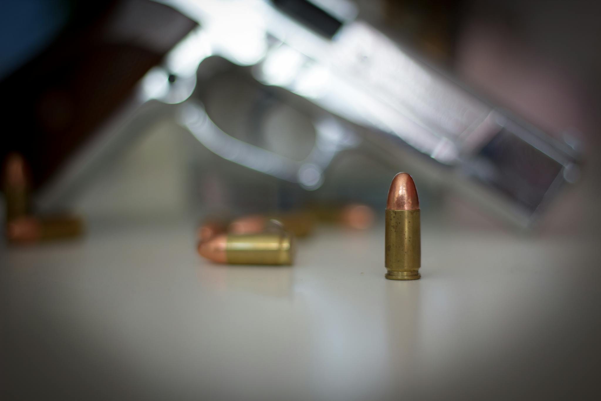 Focus on a bullet with a blurred pistol in the background, highlighting firearm accessories.
